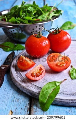Fresh red tomatoes whole and in the context of the old painted wood surface against the green salad leaves and a metal colander