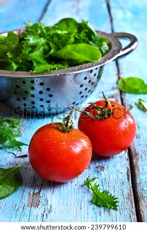 Fresh red tomatoes on old painted wood surface against the green salad leaves and a metal colander