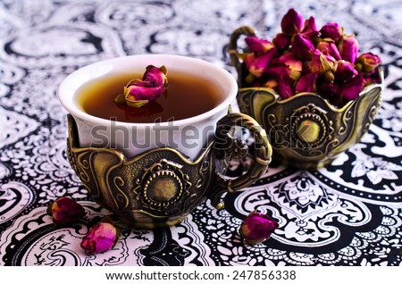 Tea in a beautiful metal Cup with Oriental motifs on the metal tray surrounded by dried rose buds