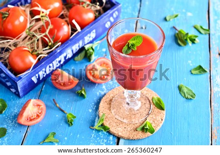 Tomato juice in a glass with mint leaves on the background of the box of tomatoes on a wooden surface