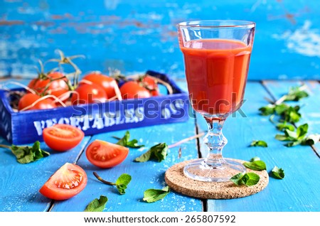 Tomato juice in a glass with mint leaves on the background of the box of tomatoes on a wooden surface