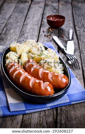 Grilled sausage with incisions with a potato side dish in a metal pan
