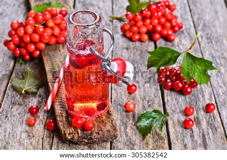 Drink red in a glass container with water drops on wooden surface on the background of viburnum berries