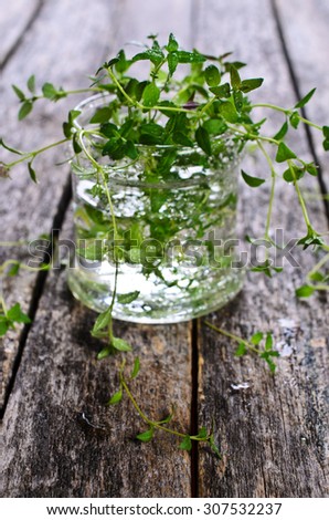 Sprigs of raw thyme with water drops in a glass container on a wooden surface