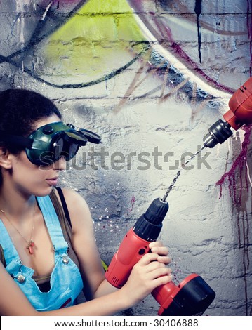 Young and beautiful girl playing with drill press near a colored grafitii wall