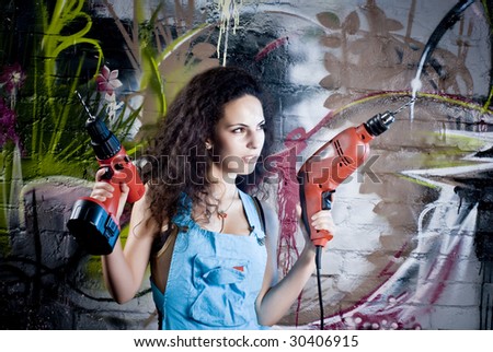 Young and beautiful girl working with drills press near a colored grafitii wall