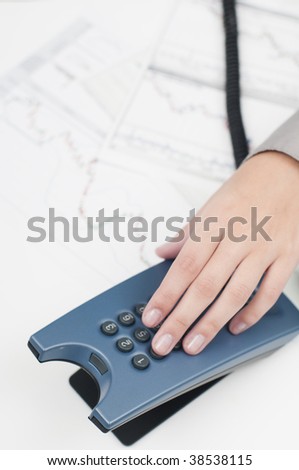 Business female hand dialing a phone number (graphs in background)