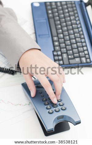 Business female hand dialing a phone number (graphs and computer keyboard in background)