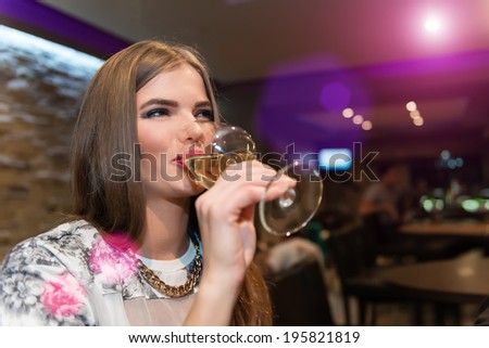 Young Woman Drinking White Wine. Happy young adult smiling and drinking white wine. Portraite image in cafe.