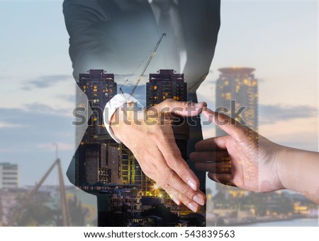Double exposure of businessman will handshaking for business relationship, construction crane and building in the evening, twilight as industrial, commitment and partnership concept.