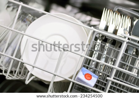 open dishwasher with clean plates in it, focus on dishwasher tabs