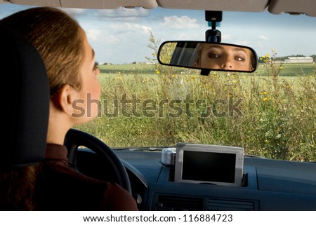 Young woman sits on driver\'s seat and Looks in the rear-view mirror.