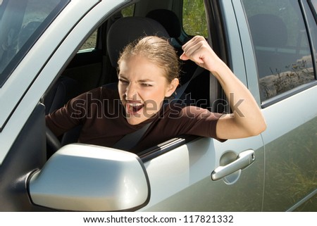 Young woman driver yelling and  shaking her fist out car window.