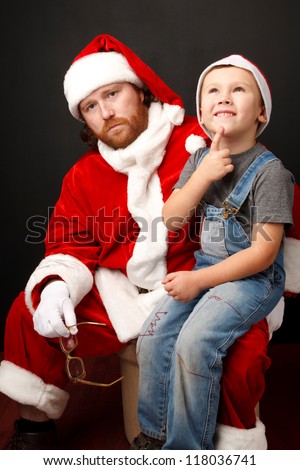 Boy is  sitting on Santas knee and thinking about his future present.  Man,dressed in Santa costume looks tired and unhappy