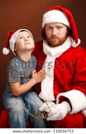 Boy is  sitting on Santas knee and asking about his future present.  Man,dressed in Santa costume looks tired and unhappy