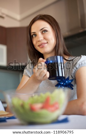 Woman is drinking her morning tea. With salad on the foreground out of focus.