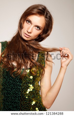 Girl in green shiny dress is holding part of her hair in hand