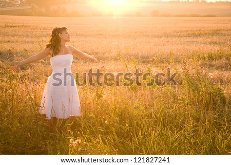 Bride on the field in the light of setting sun with her arms outstretched