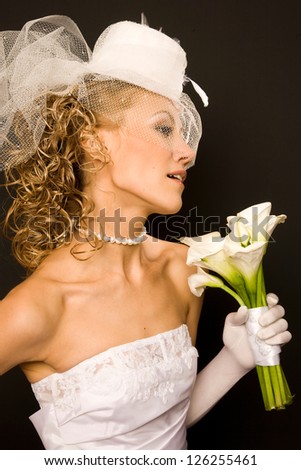 Profile of  the stunning bride dressed in retro style on the black background with the bouquet made of calla Lily