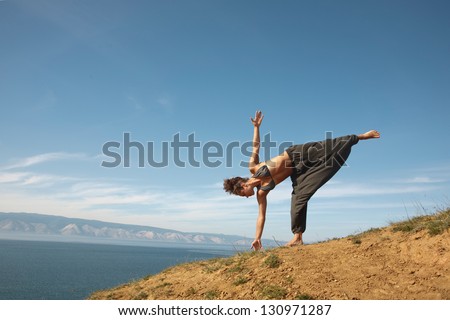 Real yoga instractor practicing on the rock near water line