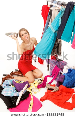 Young woman sits near her clothes rack with lots of dresses,and some clothes is on the floor,and she is holding her shoe and scream!