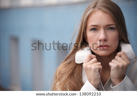 Sad young woman holding collar of her trench coat.Selective focus