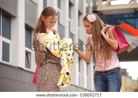 Two girls with shopping bags standing on the street,one of the girls envy of new dress another girl