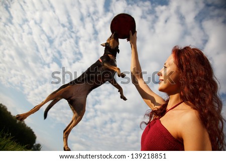 Beautiful young woman playing with her dog in park.Dog is jumping for her Frisbee