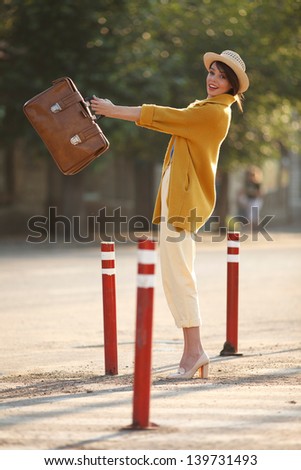 Young happy funny (vintage) dressed woman throws retro suitcase on the street near red small columns.   Picture ideal for illustating woman magazines.