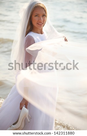 Bride is standing on the beach and holding her flying veil