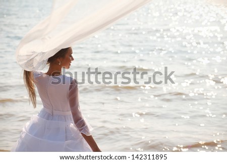 Bride with flying veil standing near shiny water