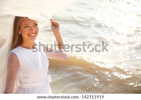 Cheerful bride near sparkling water holding her flying veil