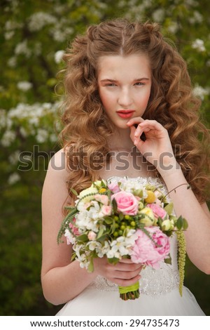Young bride with flowers stands near  blooming apple tree with colorful posy. Professional style and make-up