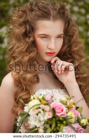 Young bride with flowers stands near  blooming apple tree with colorful posy. Professional style and make-up