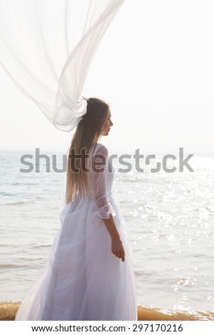 Young bride is standing near sparkling water with long flying veil.Selective focus