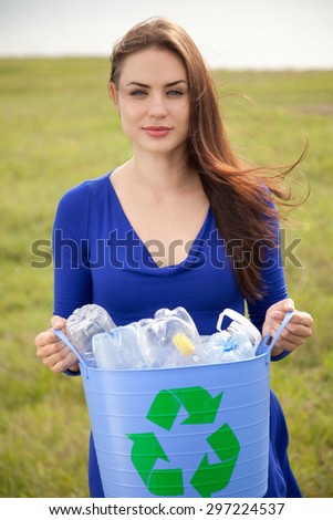Young woman holding a blue recycling bin with plastic bottles