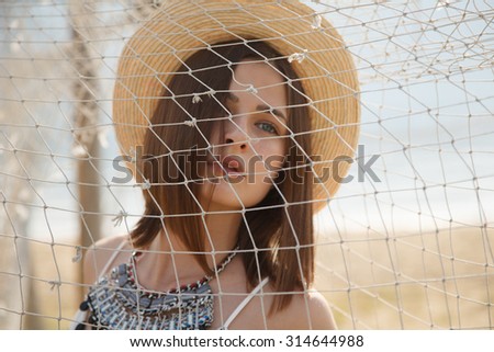 Young fashion model in straw hat  behind the fishing net outdoors near river. Professional styling,hairs, make-up