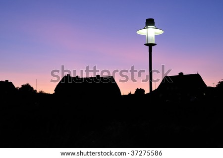 Old style artistic glowing lantern in dusk with thatched houses in background, Island of Sylt, Germany