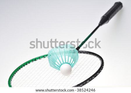 Closeup of a single badminton shuttle lying on a green and black racket, shallow DOF