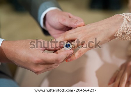 hands of a wedding heterosexual couple. Groom put a ring on finger of his lovely wife.