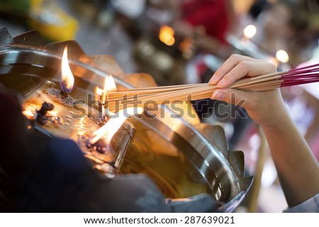 Girl grip and light the incense sticks from fire burning on oil lamp in temple