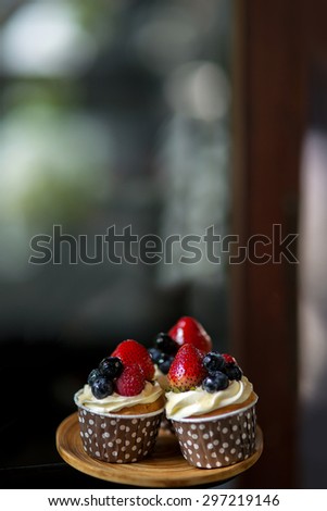 Mix of fruit berries topping on cup cake represent Strawberry , raspberries , mulberries and blueberries decorate on wooden tray