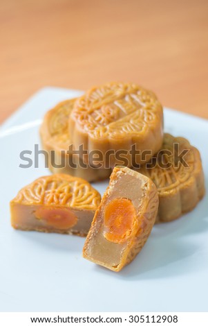 4 moon cakes in a Chinese mid-autumn festival on white plate and one cut up half to show egg yolk