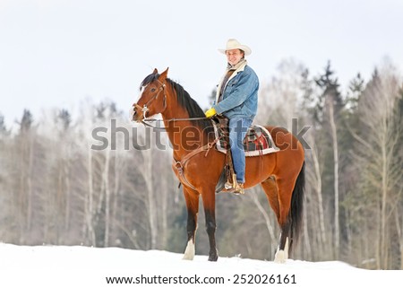 Man rides a bay horse in winter forest.