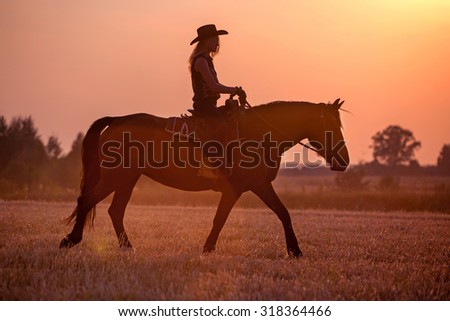 Silhouette of cowgirl riding a horse at sunset.