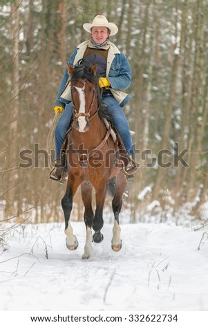 Cowboy riding bay horse in winter forest.