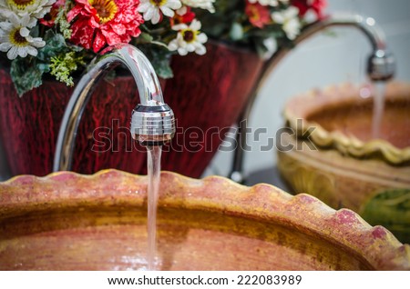 Water drop from faucet to pottery sink which have plastic flower as background