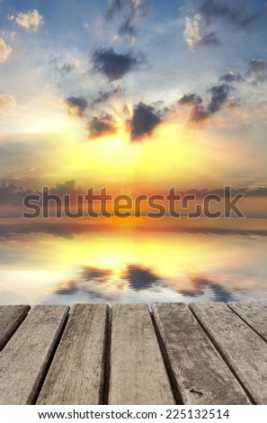 An image of old wood table have sunset sky that reflect on water as back ground