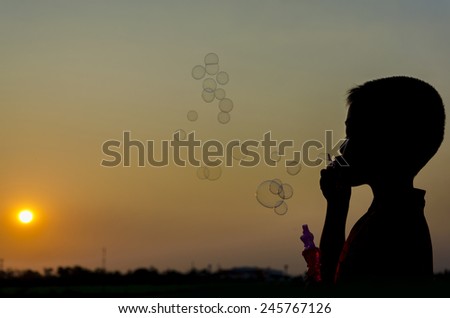 silhouette image of a boy blowing bubbles which have sunset sky as background