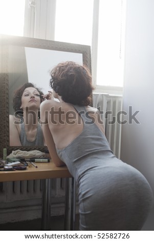 Woman kneeling while applying mascara in mirror